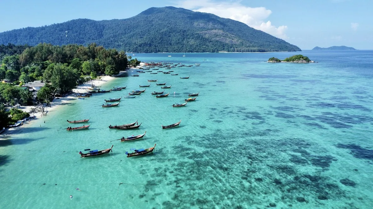 Longtail boats anchored in clear turquoise shallows off Koh Lipe with Ko Adang's green hills behind