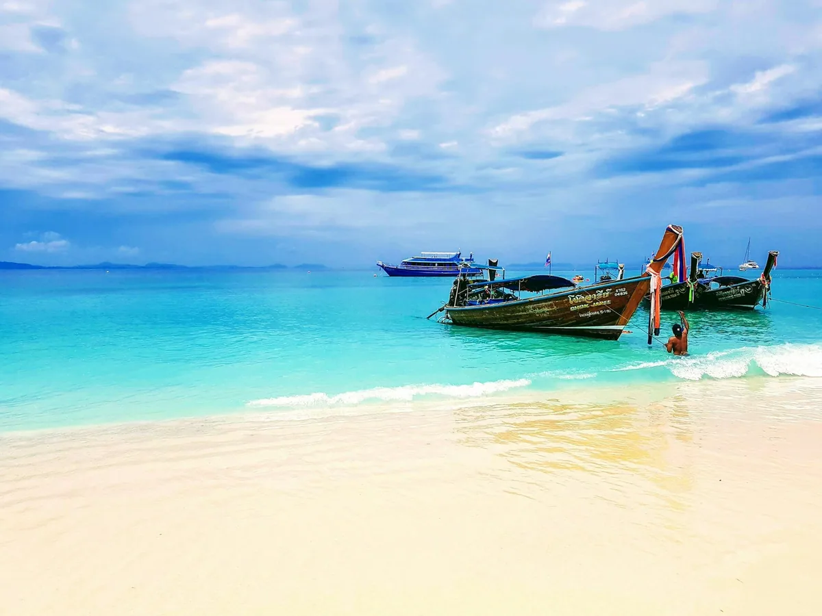 Longtail boats pulled up on a white sand beach beside turquoise water in the Phi Phi Islands